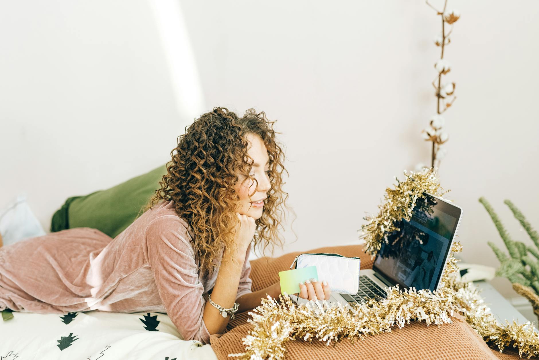 Kobieta z kręconymi włosami robi świąteczne zakupy online na laptopie