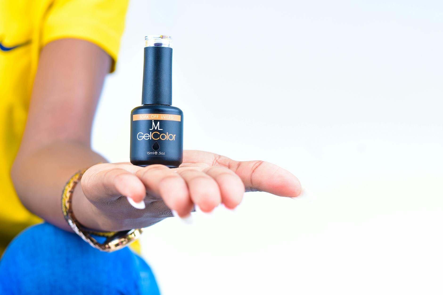 Dłoń kobiety z buteleczką lakieru hybrydowego na jasnym tle